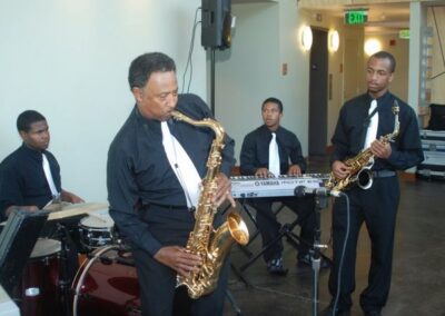 A suited man playing saxophone in a room, showcasing his musical talent and passion.